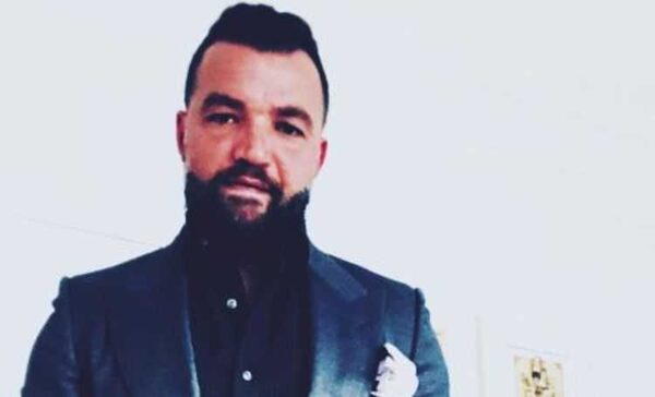 Nick E. Tarabay all suited up in grey coat and black shirt looks at the camera.